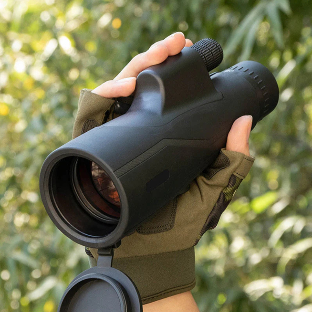 Gloved hand holding the compact monocular in the bush